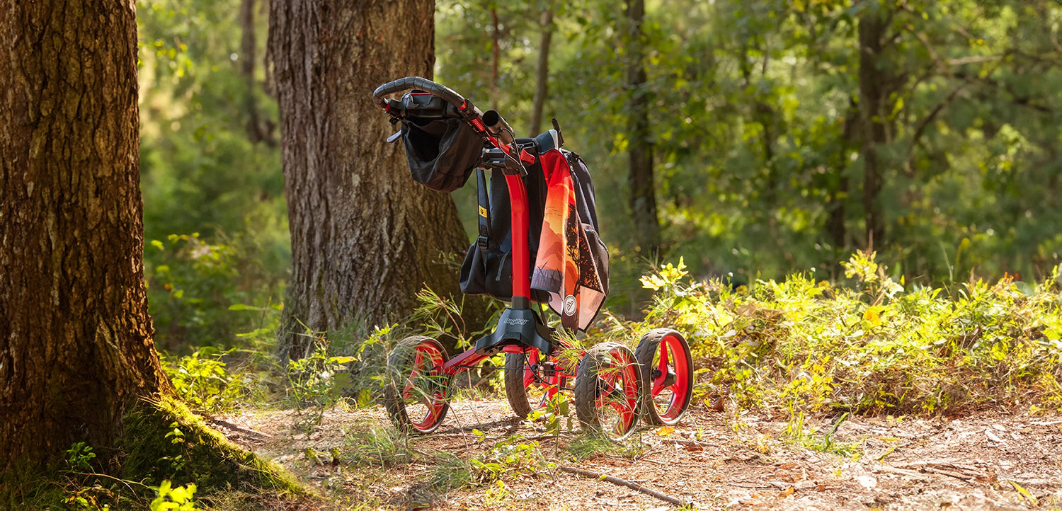 disc golf push cart with towel hanging from it in the woods