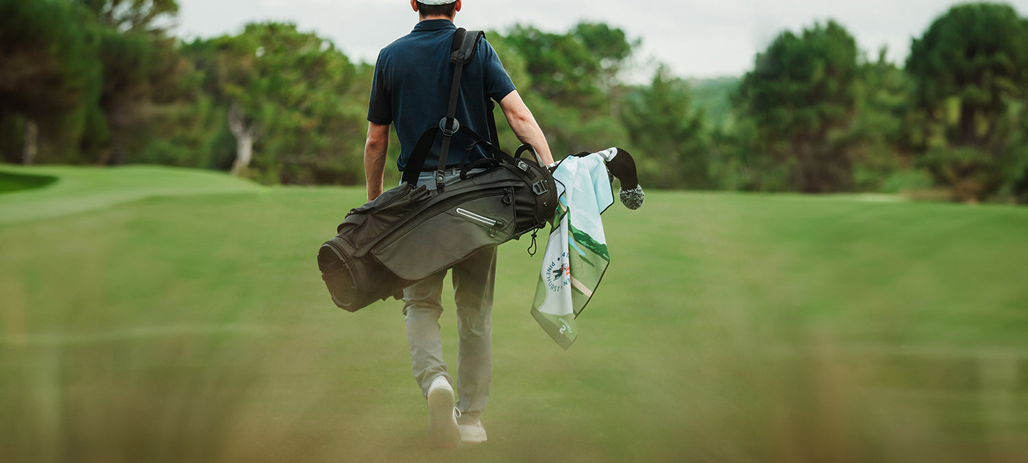 Man walking on golf course walking away carrying a golf bag on his back with U.S. Open towel hanging from it