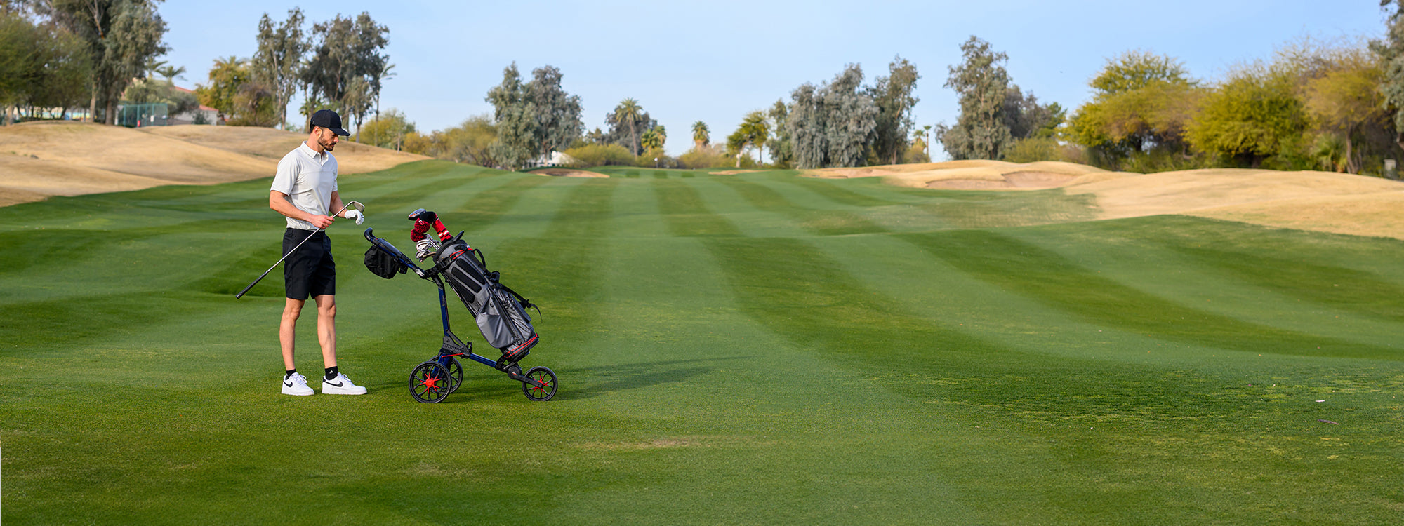 golfer on the course with a club in hand, standing beside a Nitron push cart