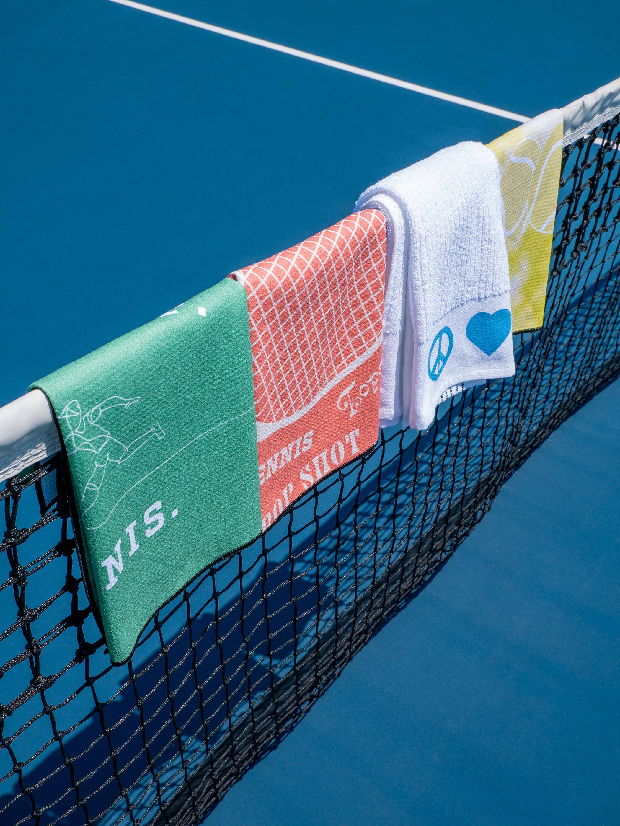 4 colorful towels hanging over tennis net, blue tennis court in background